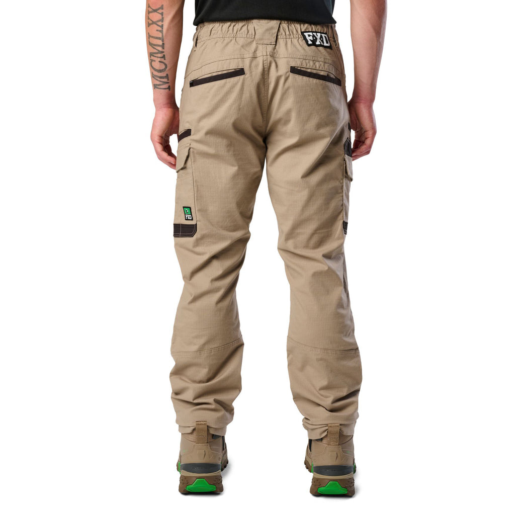 A back view of a man wearing khaki cargo style FXD Men's WP-12 Elastic Waist Stretch Ripstop Work Pants (FX02506026) with stone coloured work boots on a white background.