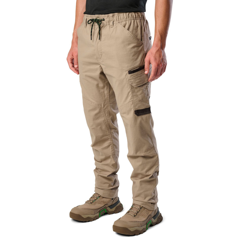 A 3-4 front view of a man wearing khaki cargo style FXD Men's WP-12 Elastic Waist Stretch Ripstop Work Pants (FX02506026) with stone coloured work boots on a white background.