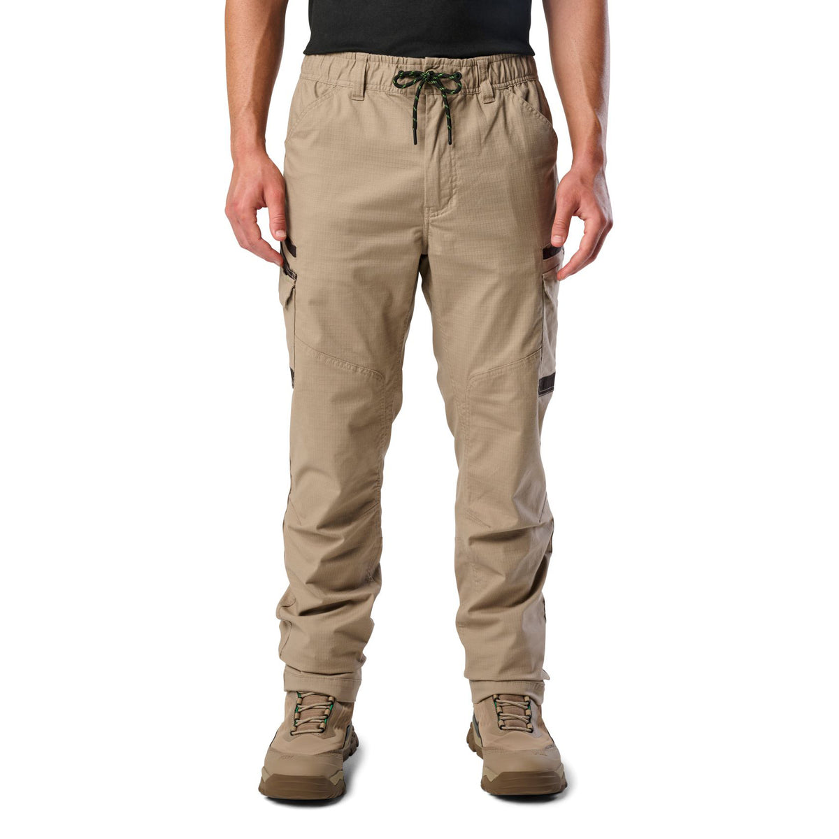 A front view of a man wearing khaki cargo style FXD Men's WP-12 Elastic Waist Stretch Ripstop Work Pants (FX02506026) with stone coloured work boots on a white background.