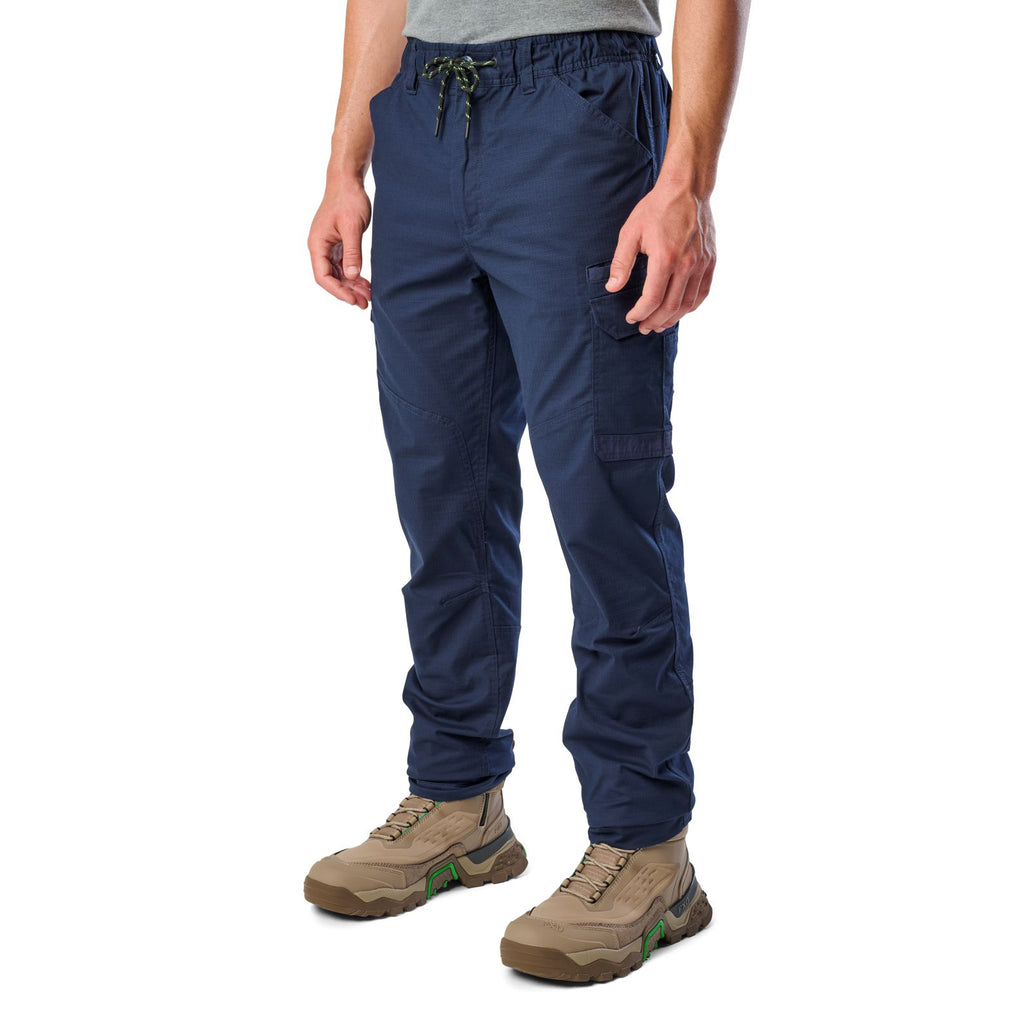 A 3-4 front view of a man wearing navy blue cargo style FXD Men's WP-12 Elastic Waist Stretch Ripstop Work Pants (FX02506026) with stone coloured work boots on a white background.