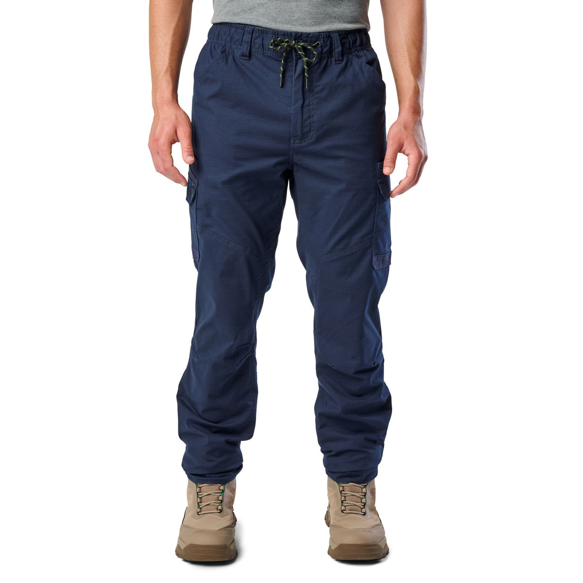 A man wearing navy blue cargo style FXD Men's WP-12 Elastic Waist Stretch Ripstop Work Pants (FX02506026) with stone coloured work boots on a white background.