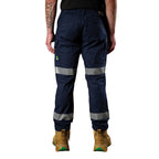 A front view of a man wearing a pair of navy blue FXD Men's WP-12T Elastic Waist Stretch Ripstop Taped Work Pants (FX02606028) with a black tee and wheat coloured work boots, on a white background.