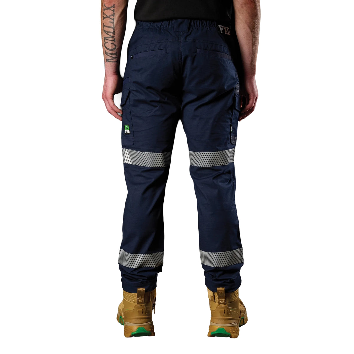 A front view of a man wearing a pair of navy blue FXD Men's WP-12T Elastic Waist Stretch Ripstop Taped Work Pants (FX02606028) with a black tee and wheat coloured work boots, on a white background.