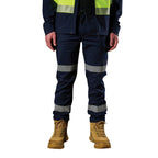A man wearing a pair of navy blue FXD Men's WP-12T Elastic Waist Stretch Ripstop Taped Work Pants (FX02606028) with a hi vis jacket and wheat coloured work boots, on a white background.