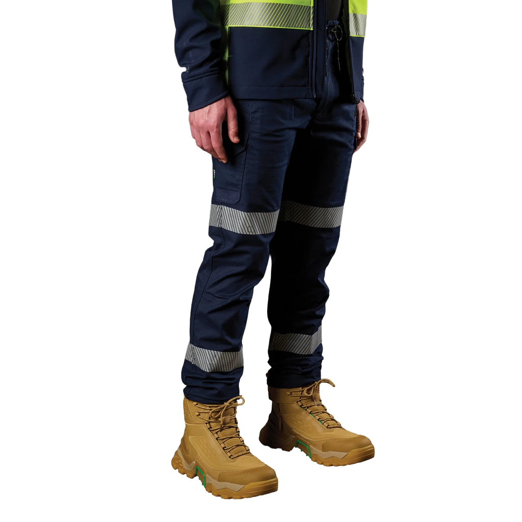 A 3-4 front view of a man wearing a pair of navy blue FXD Men's WP-12T Elastic Waist Stretch Ripstop Taped Work Pants (FX02606028) with a hi vis jacket and wheat coloured work boots, on a white background.