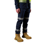 A 3-4 front view of a man wearing a pair of navy blue FXD Men's WP-12T Elastic Waist Stretch Ripstop Taped Work Pants (FX02606028) with a hi vis jacket and wheat coloured work boots, on a white background.