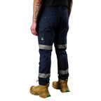 A 3-4 back view of a man wearing a pair of navy blue FXD Men's WP-12T Elastic Waist Stretch Ripstop Taped Work Pants (FX02606028) with a hi vis jacket and wheat coloured work boots, on a white background.