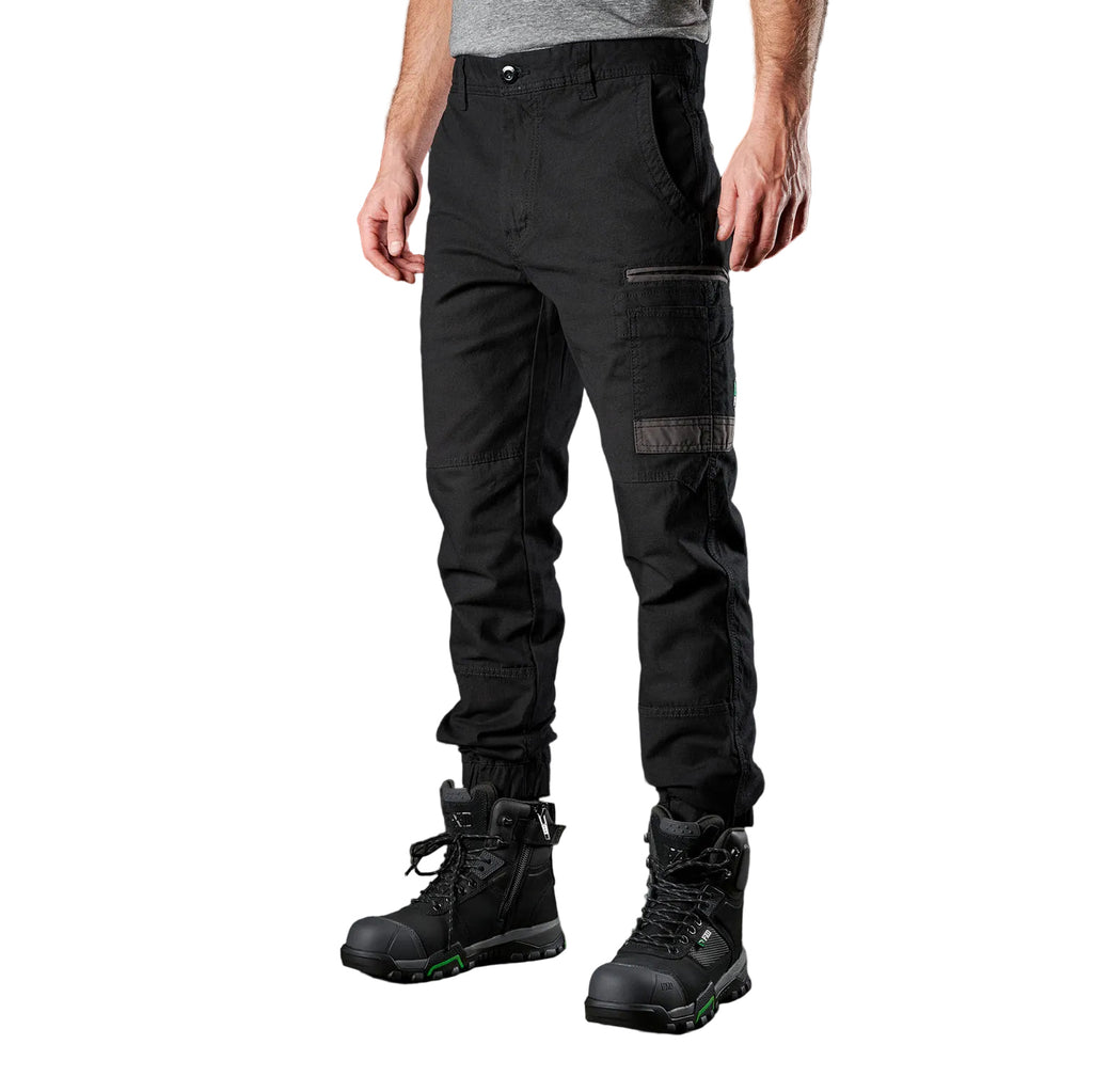 A 3-4 front view of a man wearing black FXD Men's WP-4 Stretch Cuffed Work Pants (FX01616003) with cargo pockets and elastic cuffed ankles, paired with black work boots, shown against a plain white background.