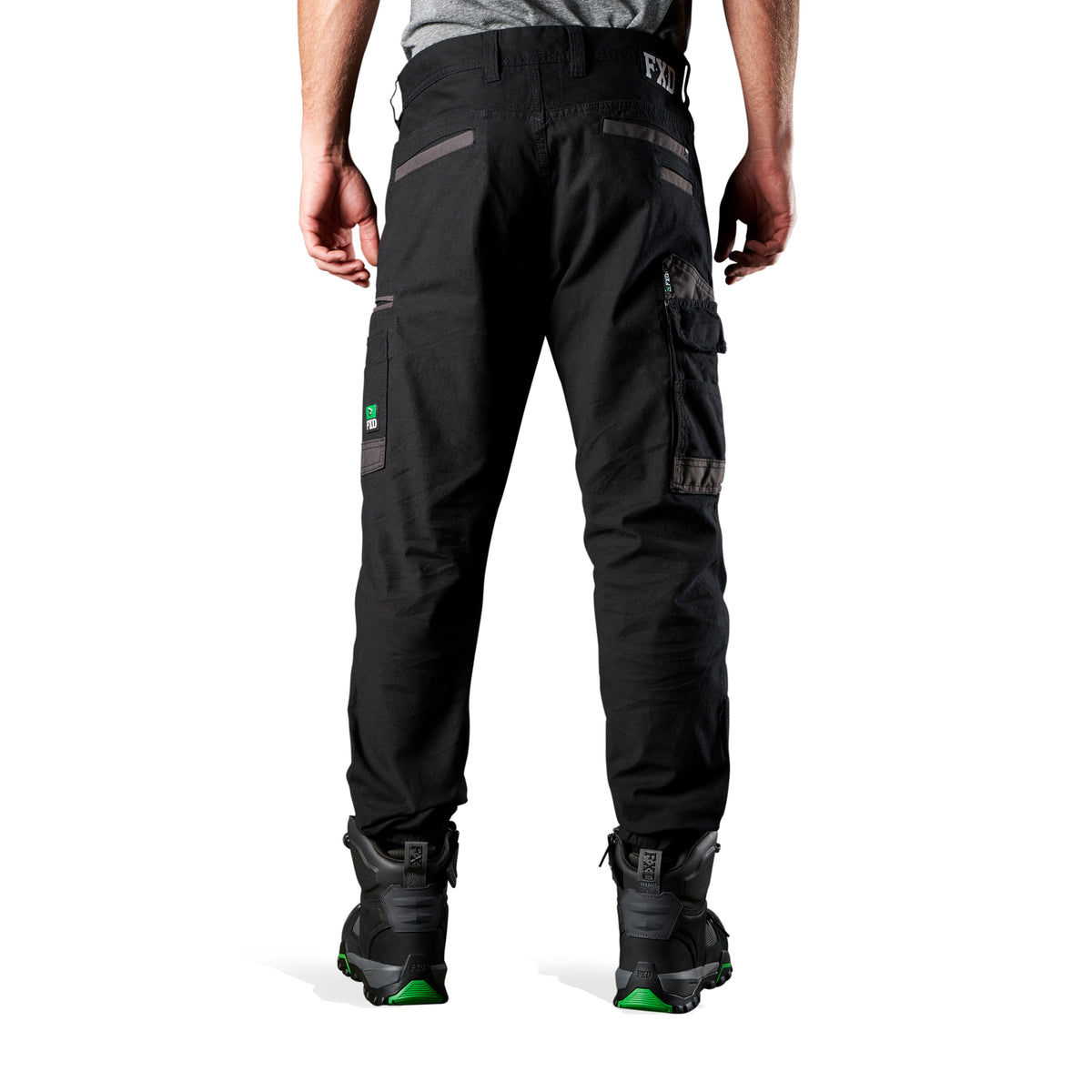 A back view of a man wearing black FXD Men's WP-4 Stretch Cuffed Work Pants (FX01616003) with cargo pockets and elastic cuffed ankles, paired with black work boots, shown against a plain white background.