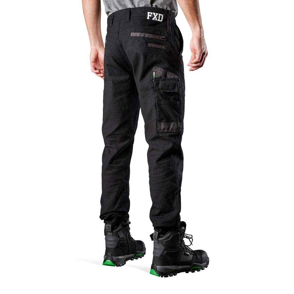 A 3-4 back view of a man wearing black FXD Men's WP-4 Stretch Cuffed Work Pants (FX01616003) with cargo pockets and elastic cuffed ankles, paired with black work boots, shown against a plain white background.