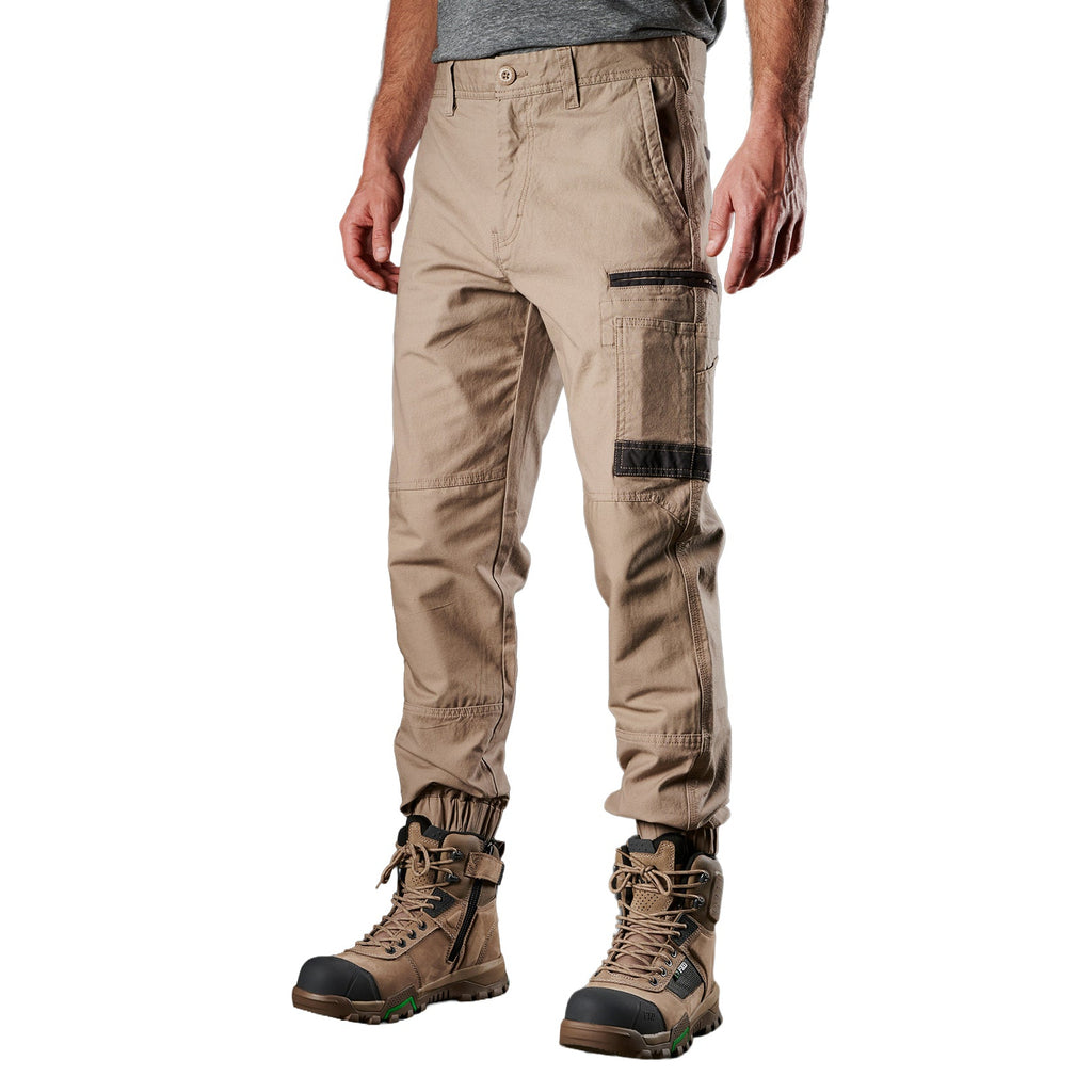 A 3-4 view of a man wearing khaki FXD Men's WP-4 Stretch Cuffed Work Pants (FX01616003) with cargo pockets and elastic cuffed ankles, paired with wheat coloured work boots, shown against a plain white background.