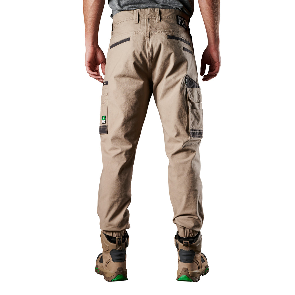 A back view of a man wearing khaki FXD Men's WP-4 Stretch Cuffed Work Pants (FX01616003) with cargo pockets and elastic cuffed ankles, paired with wheat coloured work boots, shown against a plain white background.