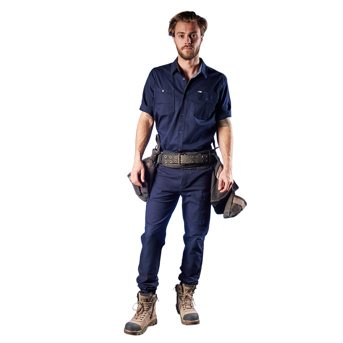 A man modelling a pair of navy FXD Men's WP-4 Stretch Cuffed Work Pants (FX01616003) with a navy FXD shirt against a plain white background, accessorized with a dark tool belt, tool pouches, and wheat coloured work boots.