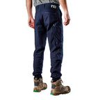 A 3-4 back view of a man wearing navy FXD Men's WP-4 Stretch Cuffed Work Pants (FX01616003) with cargo pockets and elastic cuffed ankles, paired with wheat coloured work boots, shown against a plain white background.