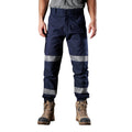 A man wearing navy blue FXD Men's WP-4T Reflective Cuffed Work Pants (FX02106017) with reflective silver bands on the legs, paired with a grey t-shirt and stone coloured work boots, against a plain white background.