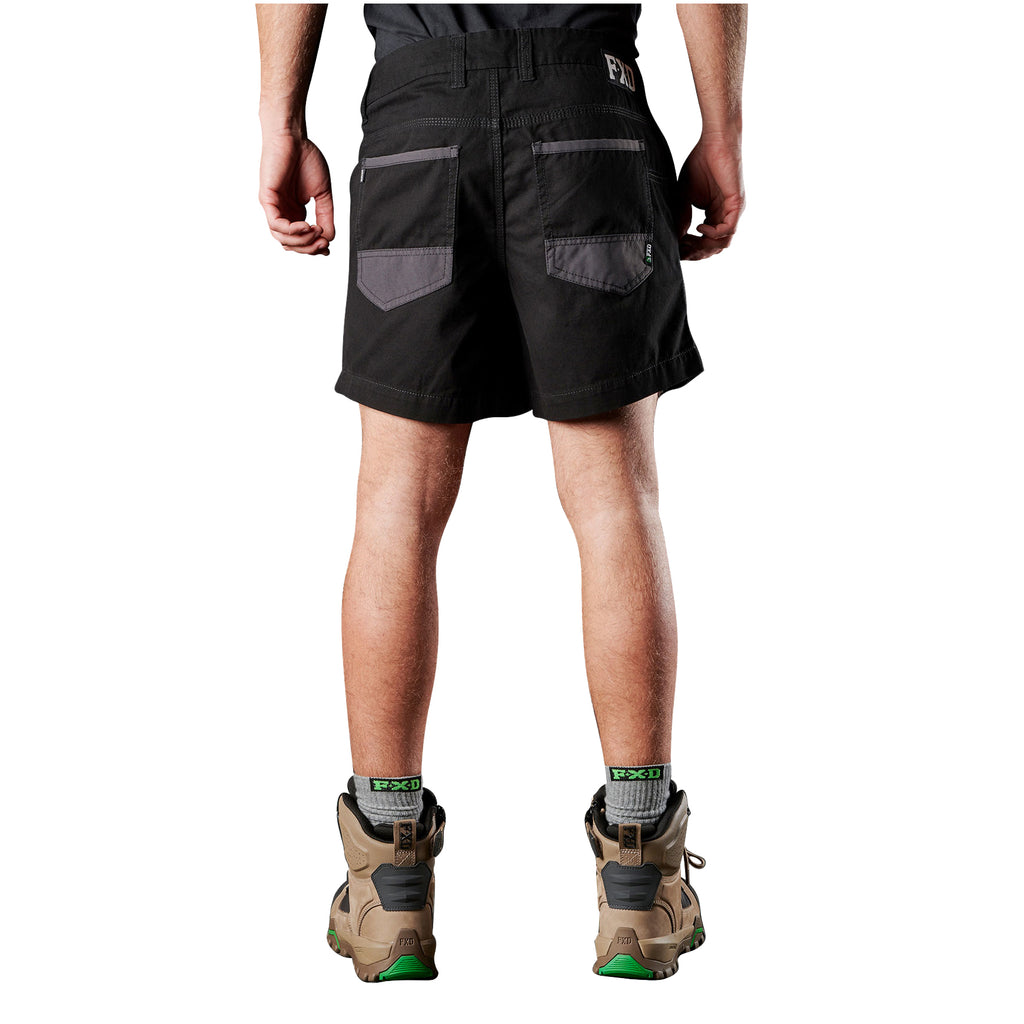 A man viewed from behind, from the waist down wearing black FXD Men's WS-2 Work Shorts (FX01136005), grey socks, and stone FXD work boots against a solid white background.