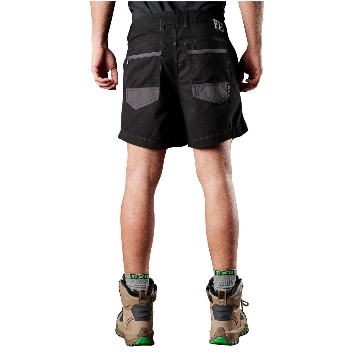 A man viewed from behind, from the waist down wearing black FXD Men's WS-2 Work Shorts (FX01136005), grey socks, and stone FXD work boots against a solid white background.