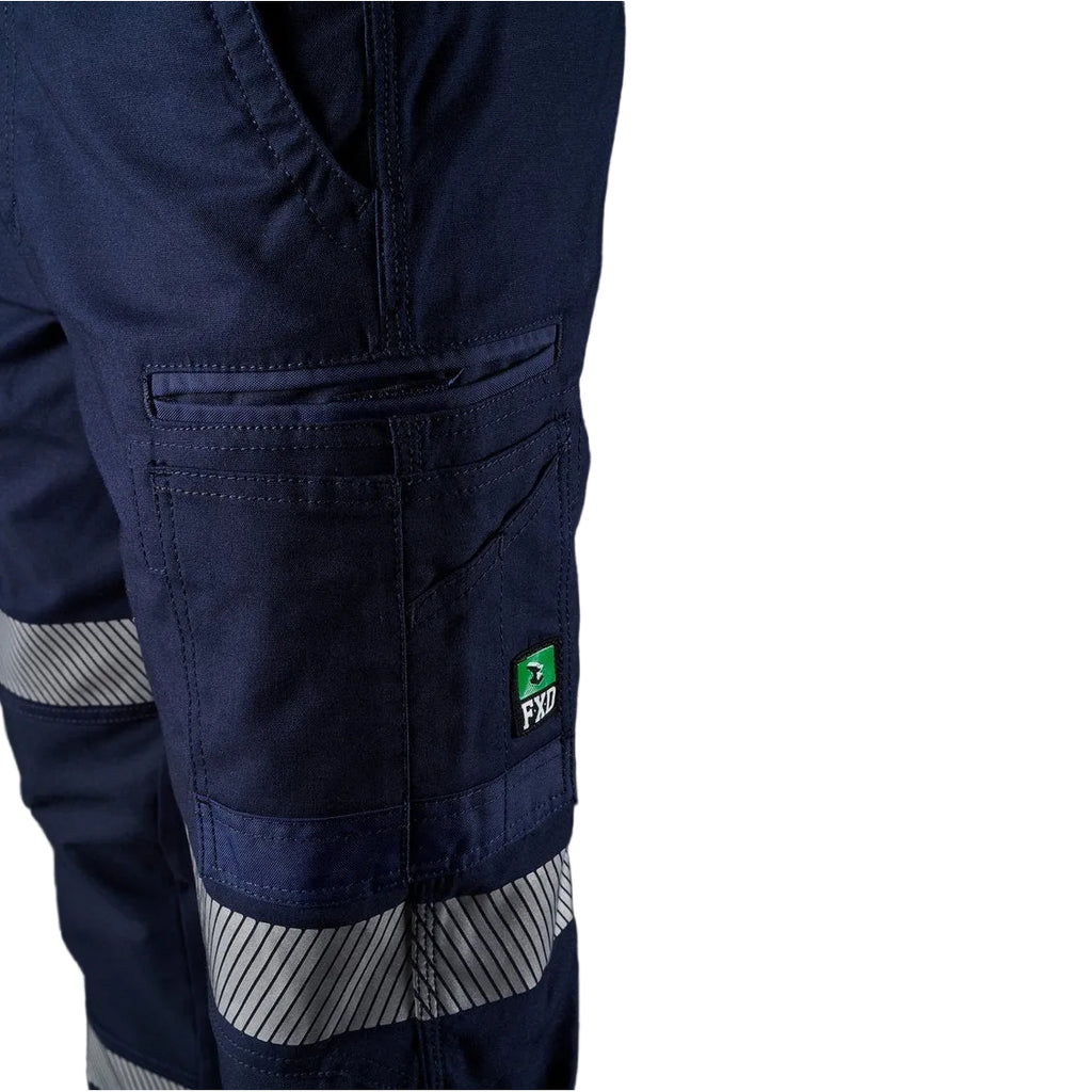 Close up pocket detail of the navy blue FXD WP-3T Reflective Stretch Work Pants (FX01906010) with reflective silver stripes on the thighs and lower legs, paired with stone coloured work boots against a white background.