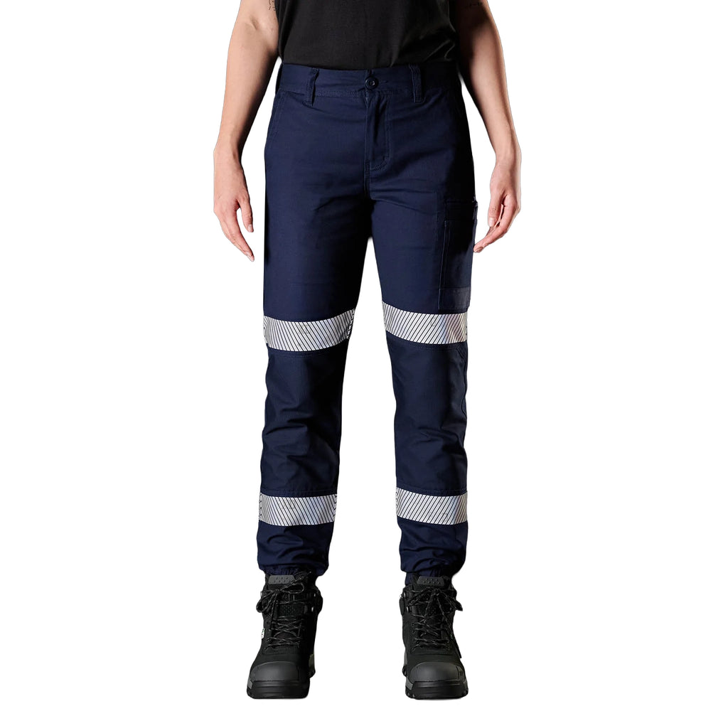 A woman wearing navy FXD Women's WP-4WT Reflective Cuffed Work Pants (FX12206208) with reflective silver stripes on the thighs and lower legs, paired with black boots against a plain white background.