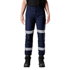A woman wearing navy FXD Women's WP-4WT Reflective Cuffed Work Pants (FX12206208) with reflective silver stripes on the thighs and lower legs, paired with black boots against a plain white background.