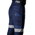 A close up side view of a woman wearing navy FXD Women's WP-4WT Reflective Cuffed Work Pants (FX12206208) with reflective silver stripes on the thighs and lower legs, paired with black boots against a plain white background.