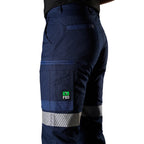 A close up side view of a woman wearing navy FXD Women's WP-4WT Reflective Cuffed Work Pants (FX12206208) with reflective silver stripes on the thighs and lower legs, paired with black boots against a plain white background.