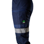 A close up side view of a woman wearing navy FXD Women's WP-4WT Reflective Cuffed Work Pants (FX12206208) with reflective silver stripes on the thighs and lower legs, paired with black boots against a plain white background.