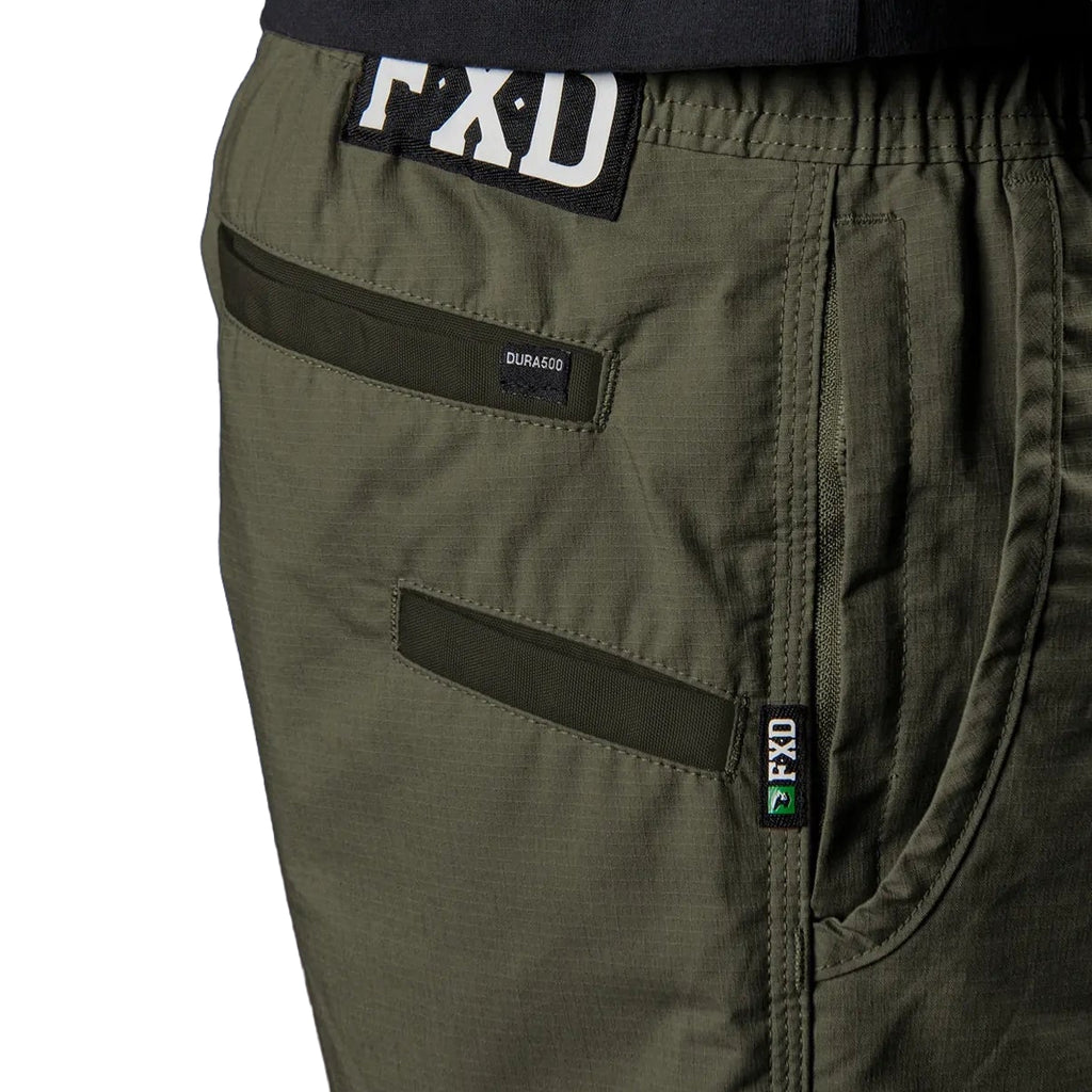 Close-up of green FXD Men's WS-4 Work Shorts (FX02006013) showing pockets, a black FXD waistband patch, and a small green FXD logo tab on the seam.