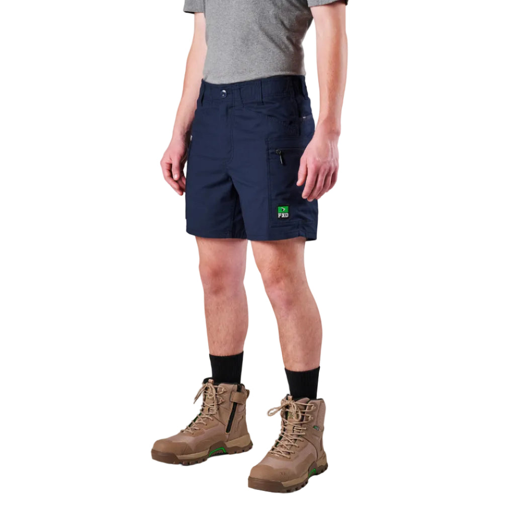 A model from the waist down wearing navy FXD Men's WS-6 Work Shorts (FX02306021), a grey tee, black crew socks, and tan work boots against a plain white background.
