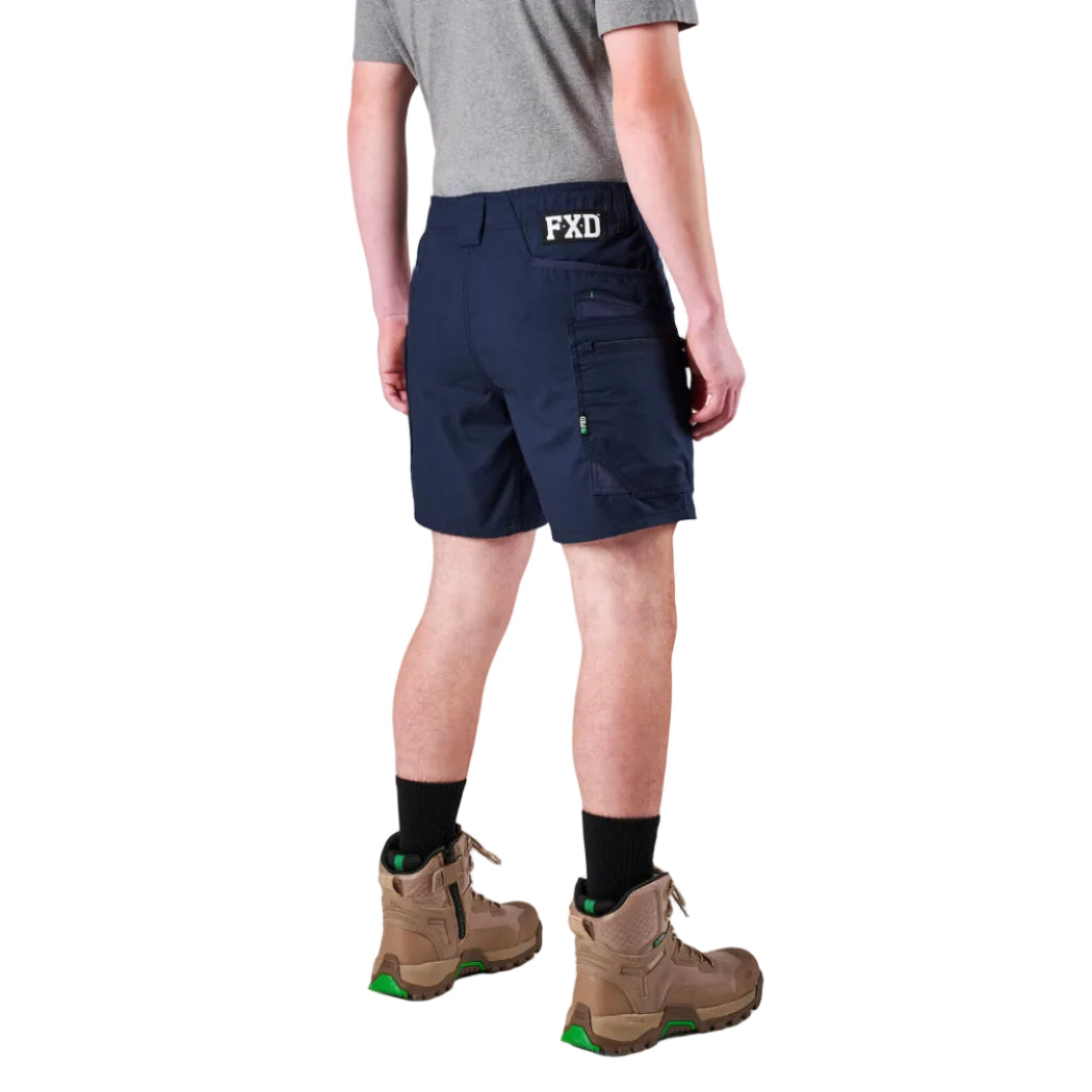 A model from the waist down wearing navy FXD Men's WS-6 Work Shorts (FX02306021), a grey tee, black crew socks, and tan work boots against a plain white background.