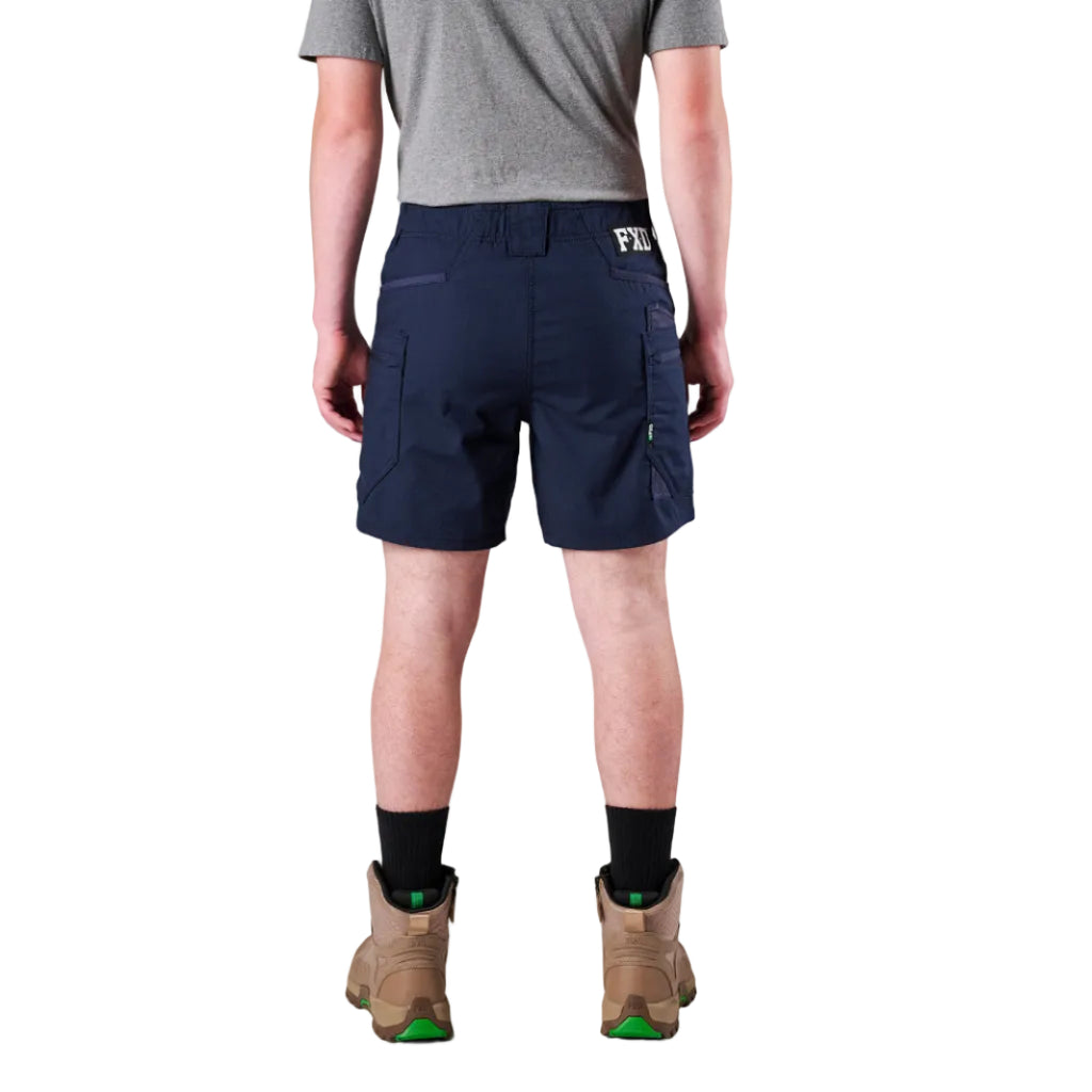 A model from the waist down wearing navy FXD Men's WS-6 Work Shorts (FX02306021), a grey tee, black crew socks, and tan work boots against a plain white background.