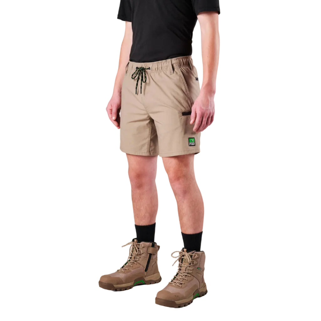A man modelling khaki FXD Men's WS-7 Work Shorts (FX02306022) with a black tee, black crew socks and stone coloured boots on a white background.