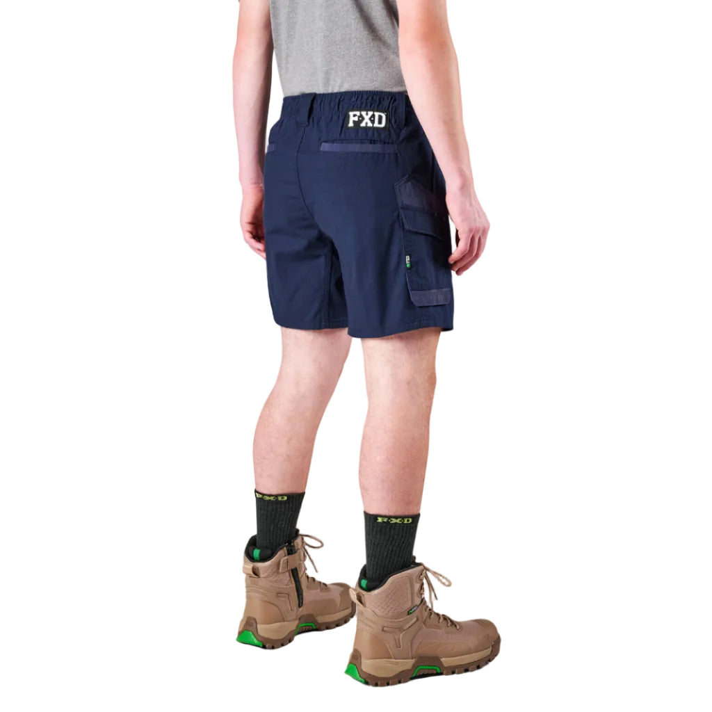 A man modelling navy FXD Men's WS-7 Work Shorts (FX02306022) with a grey tee, black crew socks and stone coloured boots on a white background.