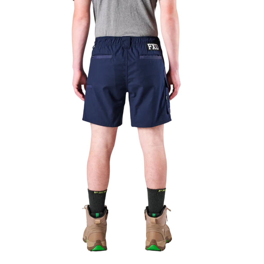 A man modelling navy FXD Men's WS-7 Work Shorts (FX02306022) with a grey tee, black crew socks and stone coloured boots on a white background.