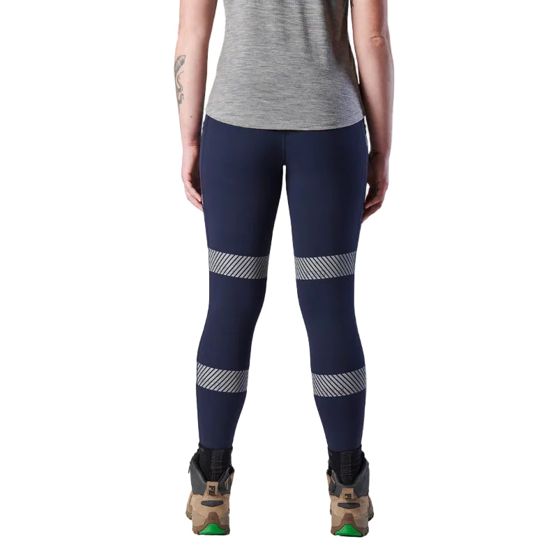 A back view of a woman wearing a pair of navy FXD Women's Taped Work Leggings (WP-9WT) paired with a grey tee and stone coloured work boots.