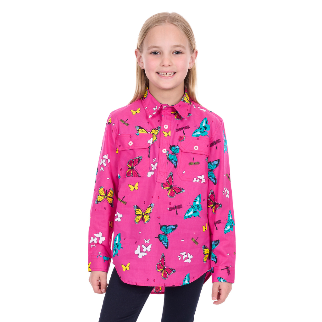 A young girl with long blonde hair smiles in a Hard Slog Childrens Giselle Half Button L/S Shirt (H6W7101169) in hot pink, paired with dark pants, standing against a white background.
