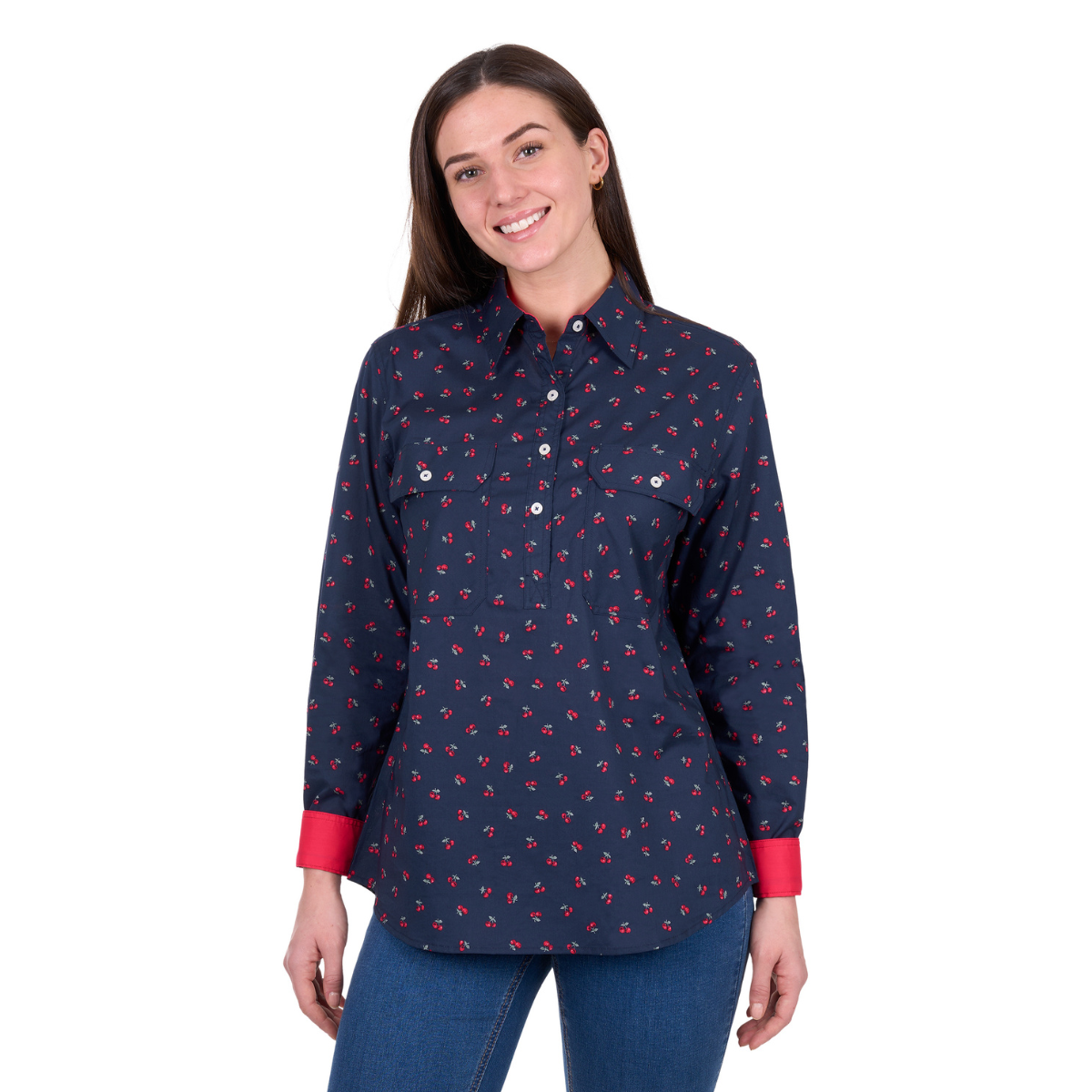 A woman in the Hard Slog Womens Cherry Half Button L/S Shirt (Dark Navy, H6W2101175)—a 100% cotton long sleeve by Hard Slog with a small red and white print—smiles at the camera in blue jeans against a white background.