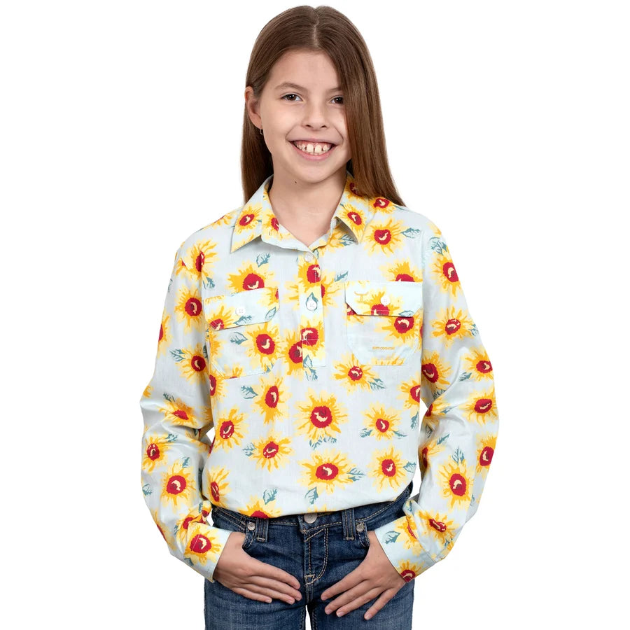 A young girl smiling and wearing a long-sleeve Just Country Girls Harper Half Button Long Sleeve Print Shirt (GWLS2278) western-style with a yellow sunflower print on a white background, paired with blue jeans, against a plain white studio background.