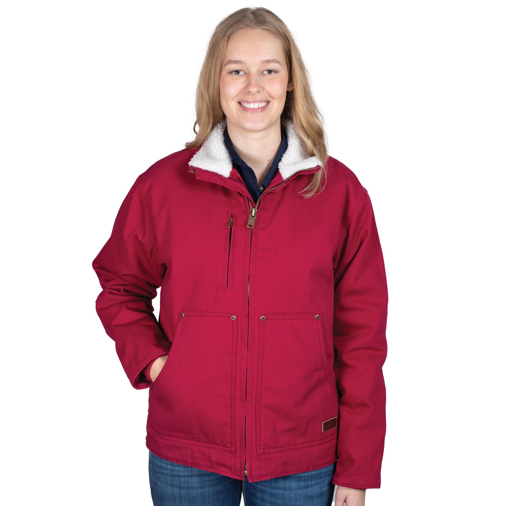 A person with long blonde hair smiles while wearing the Just Country Unisex Diamantina Sherpa Jacket (MWOJ2601) in Very Berry, paired with blue jeans, standing against a plain white background.