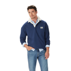 A man in the R.M.Williams Mens Classic R.M.W Rugby (KR200RJ18) Vintage Blue shirt, layered over a light blue button-down and blue jeans, stands with one hand in his pocket against a plain white background.