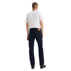 A man with his back to the camera wearing dark blue rinse Levi's Men's 517 Heritage Bootcut Jeans (00517-0216), a white t-shirt, and black shoes, standing against a solid white background.
