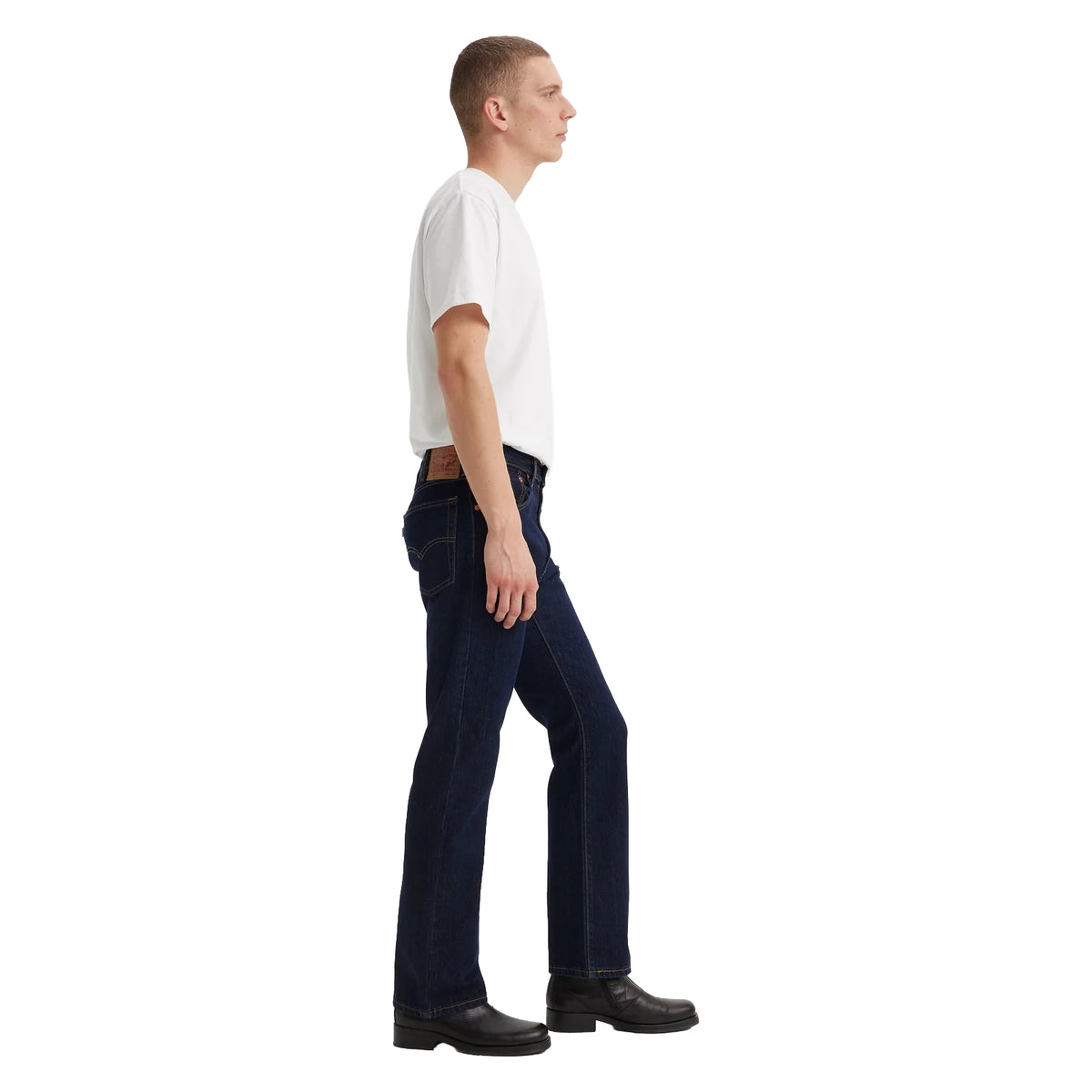 A man in profile wearing dark blue rinse Levi's Men's 517 Heritage Bootcut Jeans (00517-0216), a white t-shirt, and black shoes, standing against a solid white background.