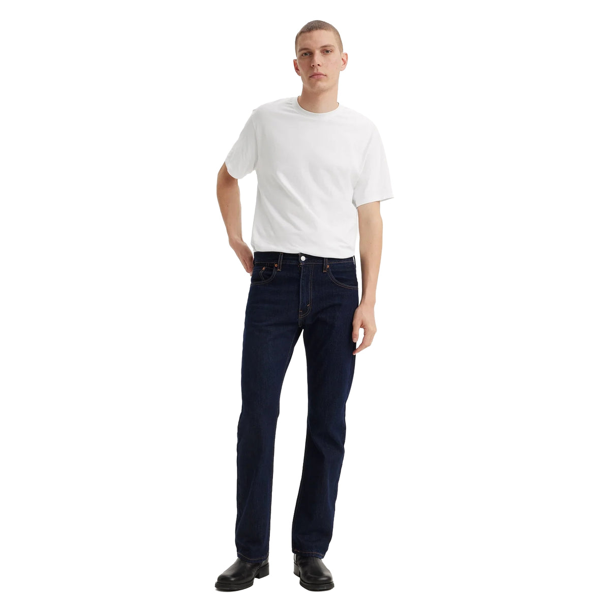 A man wearing dark blue rinse Levi's Men's 517 Heritage Bootcut Jeans (00517-0216), a white t-shirt, and black shoes, standing against a solid white background.