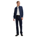 A man wearing dark blue rinse Levi's Men's 517 Heritage Bootcut Jeans (00517-0216), a white t-shirt, a denim jacket and black shoes, standing against a solid white background.