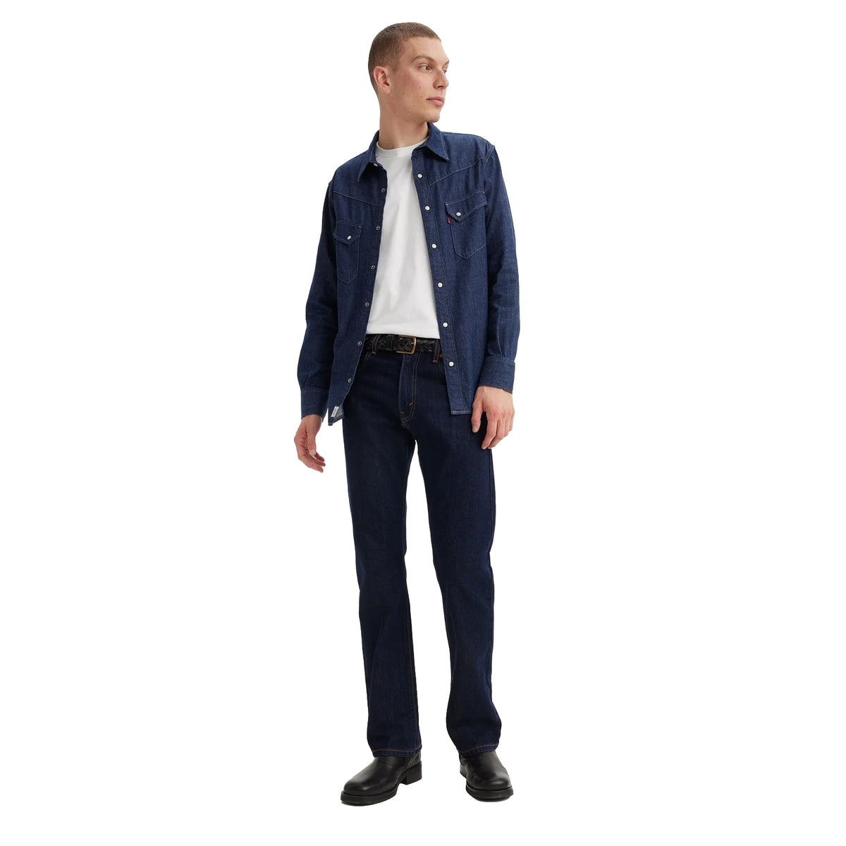 A man wearing dark blue rinse Levi's Men's 517 Heritage Bootcut Jeans (00517-0216), a white t-shirt, a denim jacket and black shoes, standing against a solid white background.