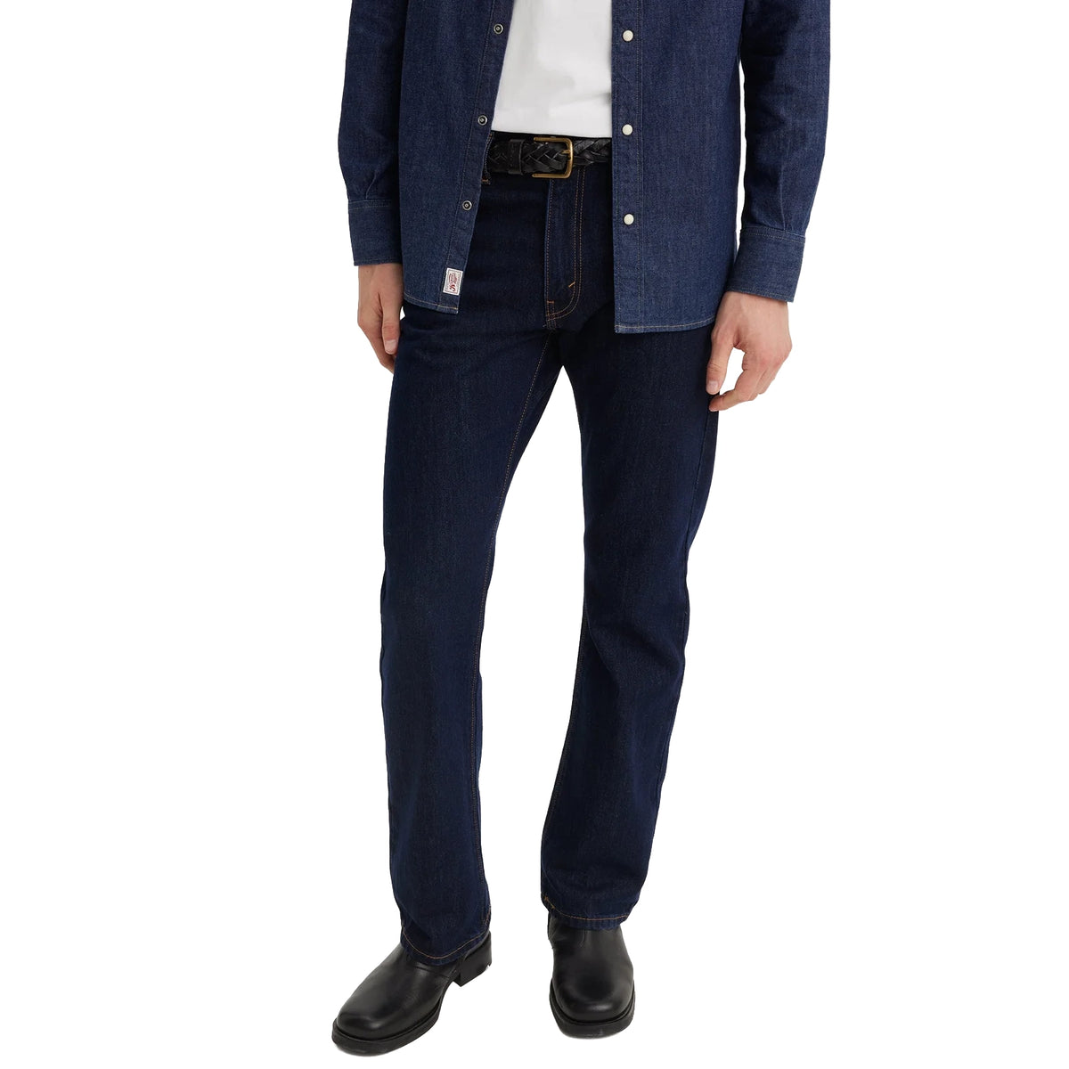 A man from the waist down wearing dark blue rinse Levi's Men's 517 Heritage Bootcut Jeans (00517-0216), a white t-shirt, denim jacket and black shoes, standing against a solid white background.