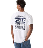 A man with short curly hair wears a Levi's Men's Graphic S/S Tee (16143-2384) Archival Cowboy 1 White—a relaxed fit, white tee with a large blue "LEVI'S THE ORIGINAL" graphic and oval image on the back—paired with blue jeans.