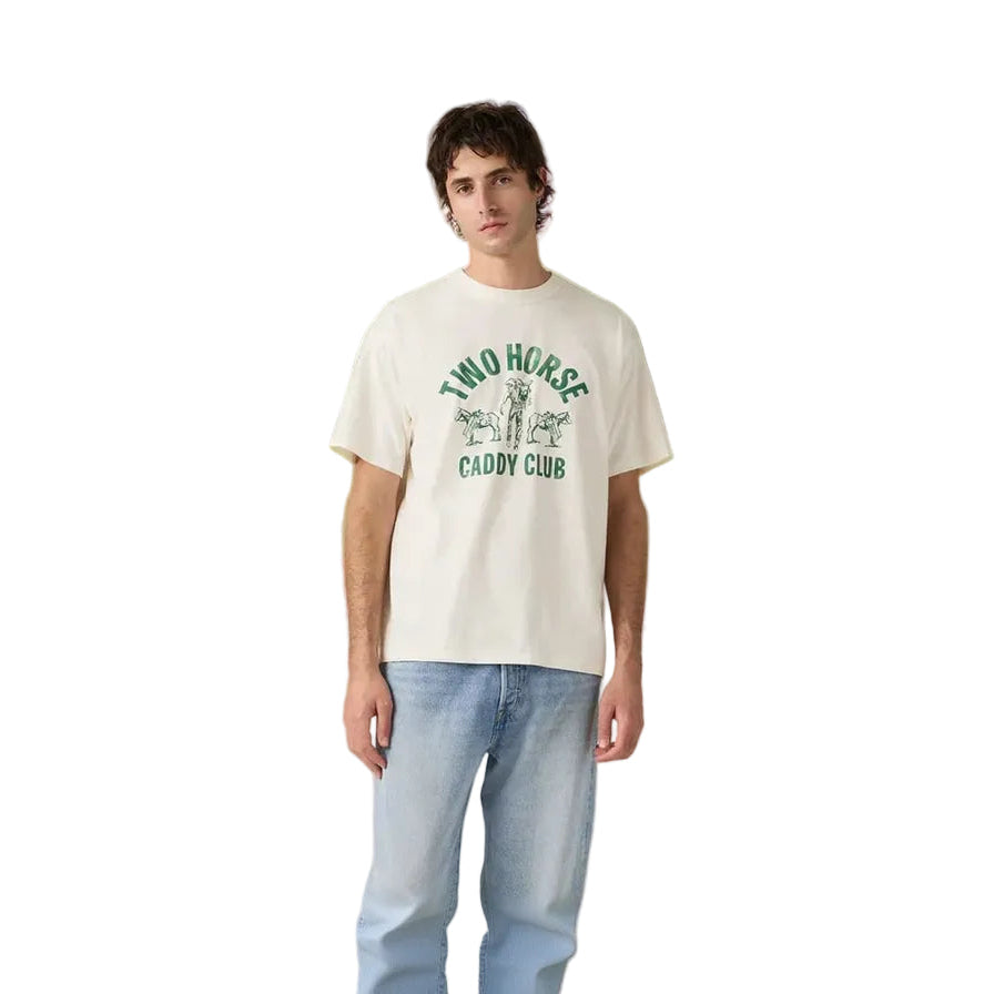 A young man wears light blue jeans and a Levi's Men's Graphic S/S Tee (87373-0410) Two Horse Caddy Club Egret, featuring vintage green text and horse graphic, standing against a plain white background.