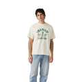 A young man wears light blue jeans and a Levi's Men's Graphic S/S Tee (87373-0410) Two Horse Caddy Club Egret, featuring vintage green text and horse graphic, standing against a plain white background.