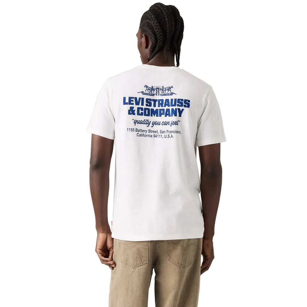 A man viewed from behind wearing a white Levi's t-shirt with a blue graphic print on the back, paired with khaki pants, against a white studio background.